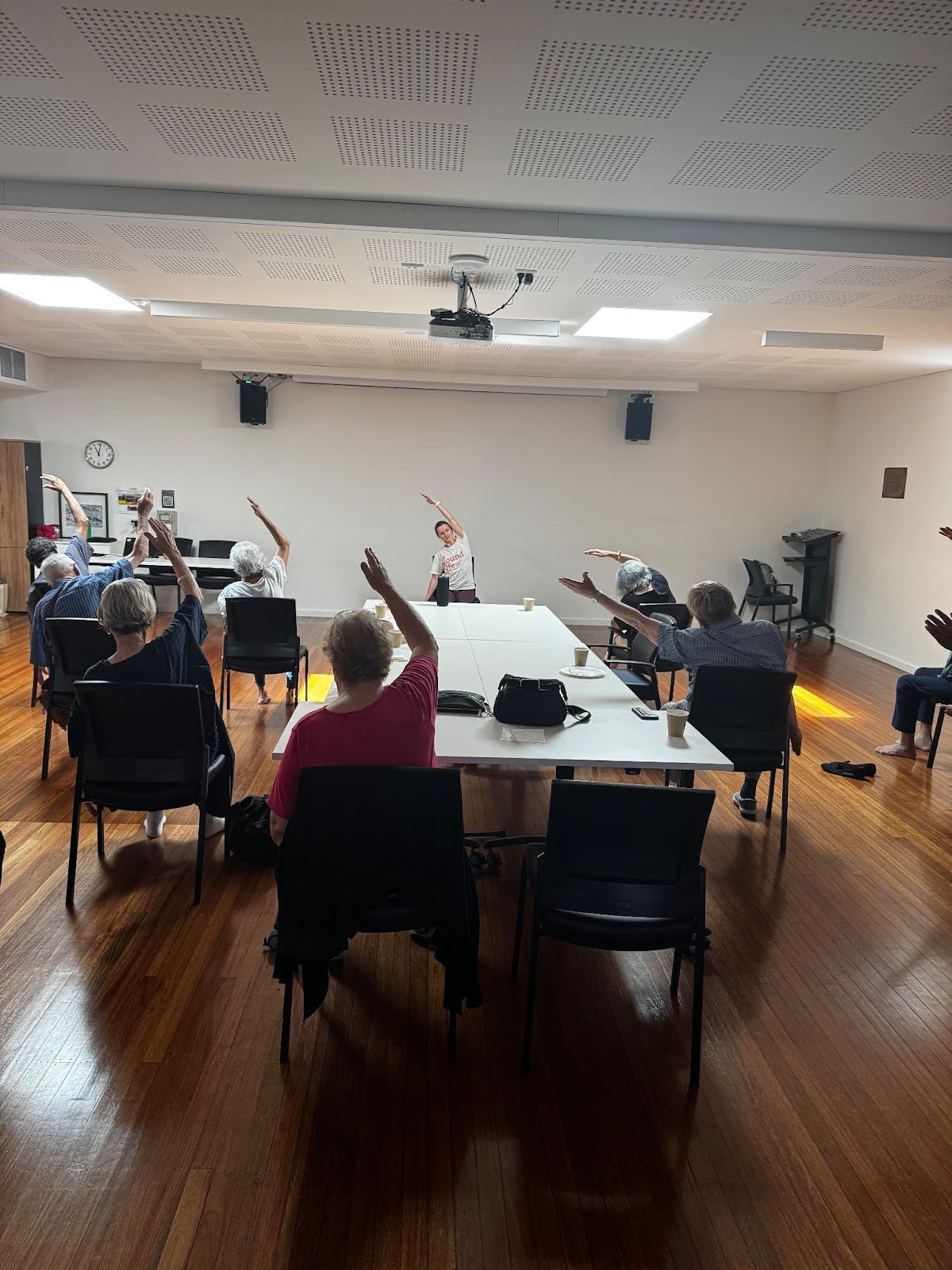 Older adults doing seated chair yoga with an A Sound Life teacher in a community room