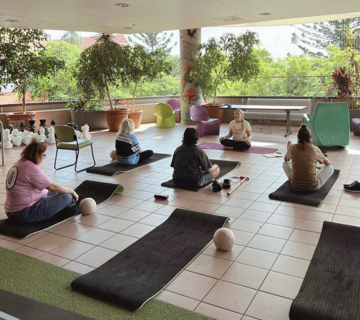 A small group practising seated yoga with an A Sound Life teacher on an outdoor terrace surrounded by plants