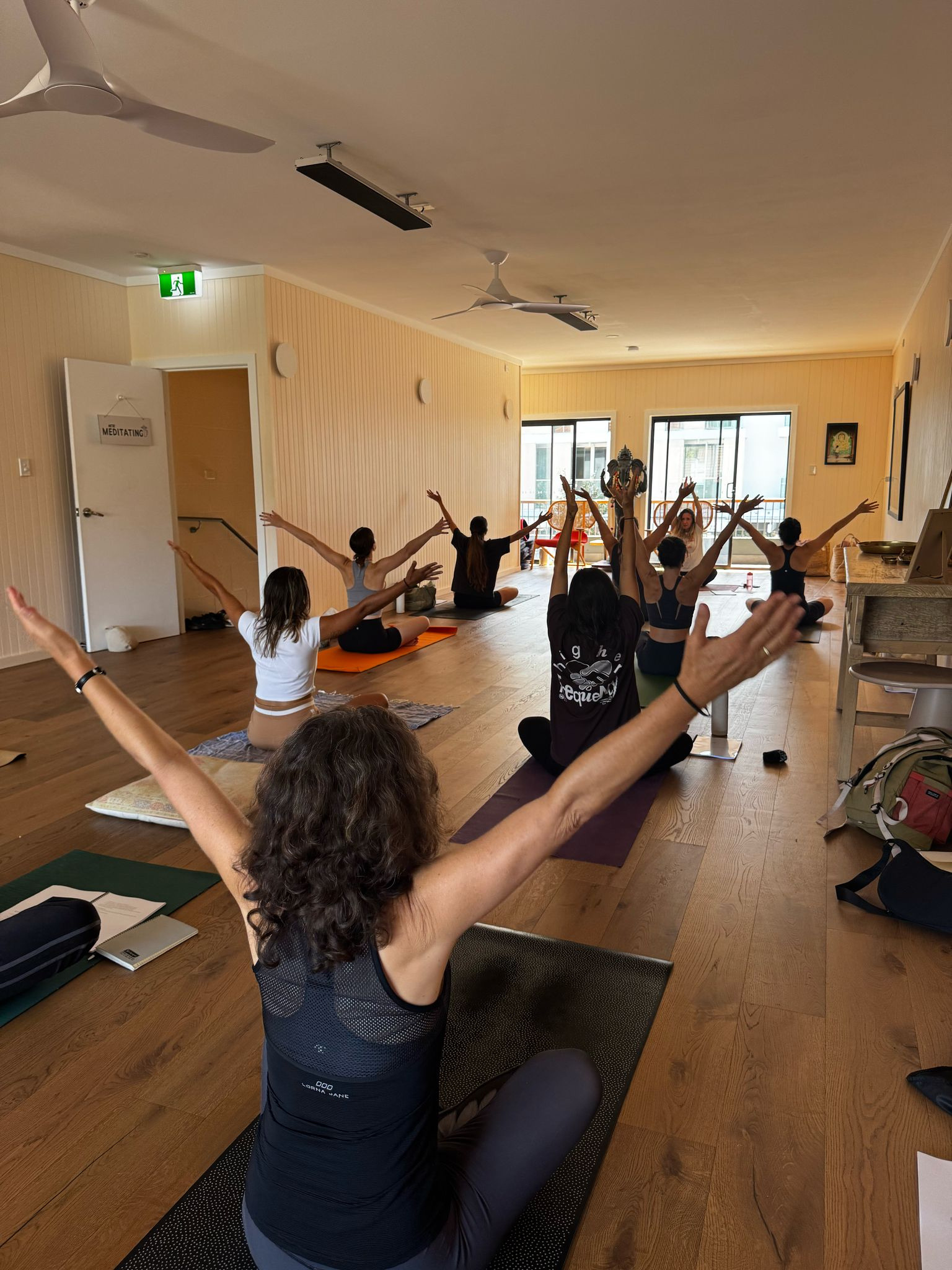 A yoga class seen from behind, everyone stretching their arms wide