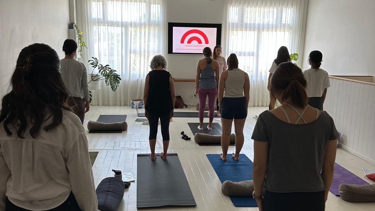 Yoga teachers standing on mats during A Sound Life's trauma-aware yoga teacher training, facing a screen reading Trauma Aware Yoga